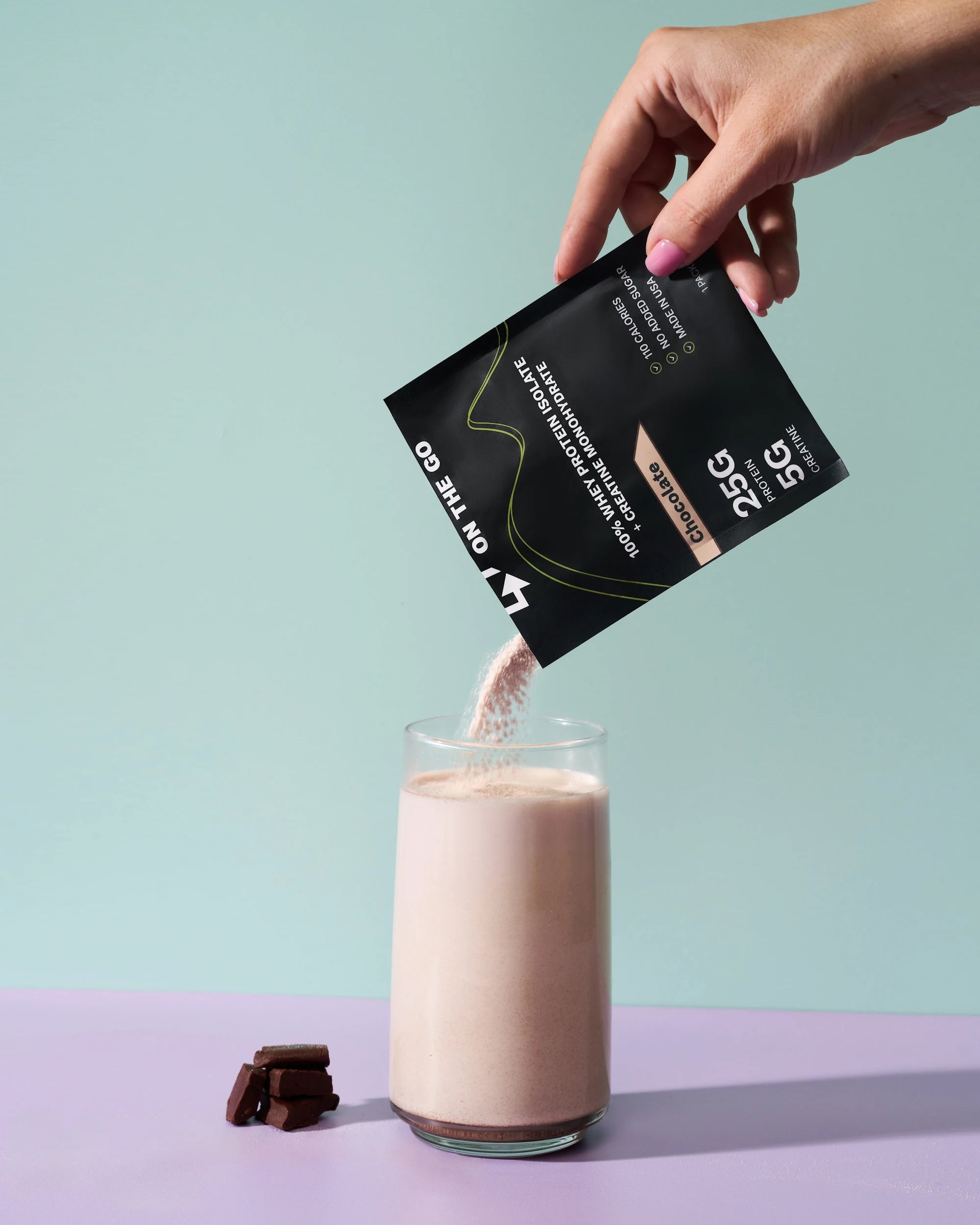 Hand pouring a protein powder mix into a glass of milk with a green and purple gradient background.