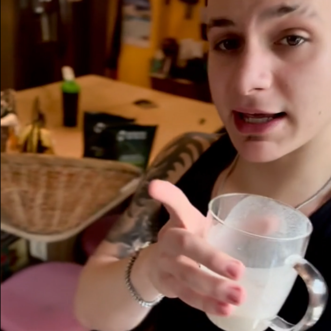 Person holding a clear mug with a white liquid in a casual indoor setting