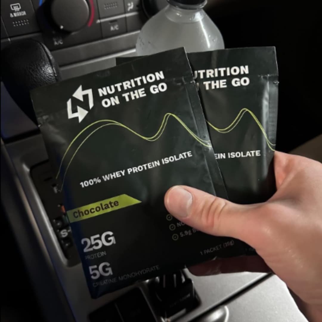Two packages of &#39;Nutrition on the Go&#39; 100% Whey Protein Isolate held by a hand in a car.