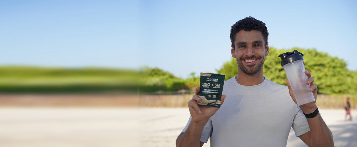 Gabe, founder of Nutrition On The Go, holding a protein + creatine packet and a shaker at the beach