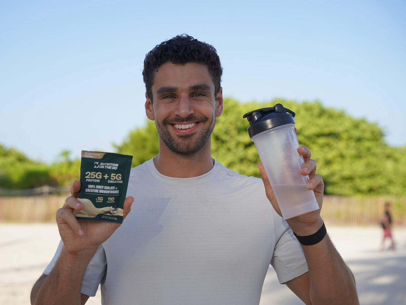 Holding a mixed shaker and a Nutrition On The Go packet at the beach
