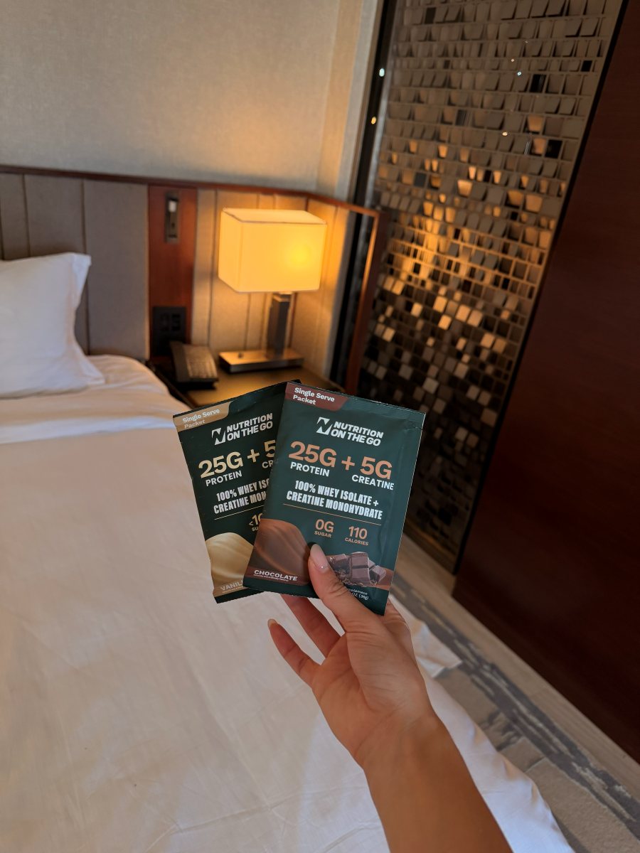 Hand holding two Nutrition On The Go packets in a hotel room